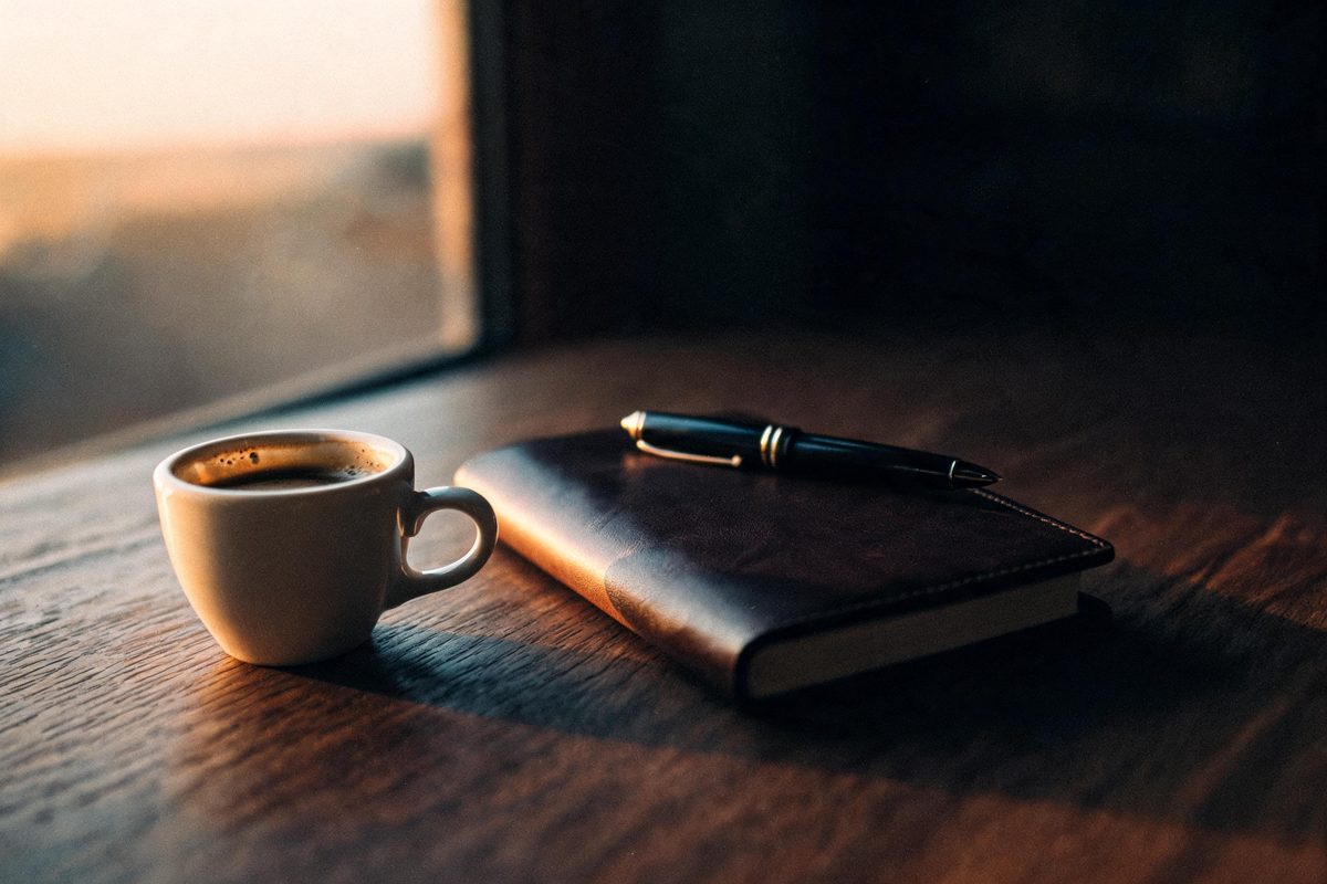 Espressotasse, Notizbuch und Stift auf einem dunklen Holztisch