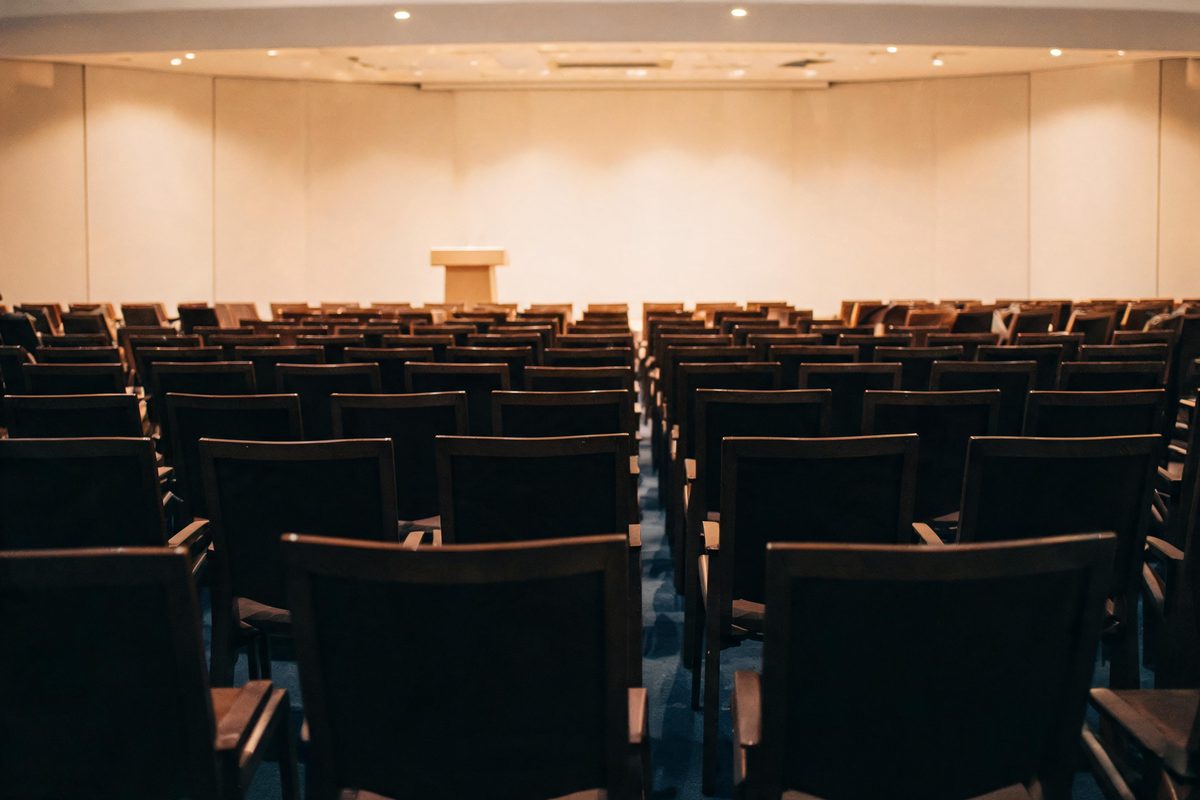 Leere Stuhlreihen vor einem Rednerpult in einem Saal